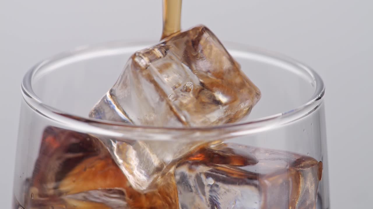 cerca de cola fresca que se vierte en el vaso con cubos de hielo en fondo blanco