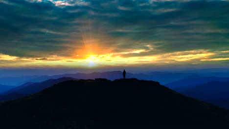 the male silhouette on the mountain against the bright sunset background