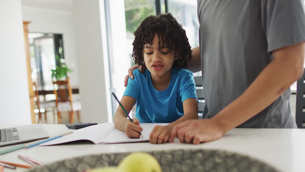 hombre biracial feliz y su hijo haciendo la tarea juntos
