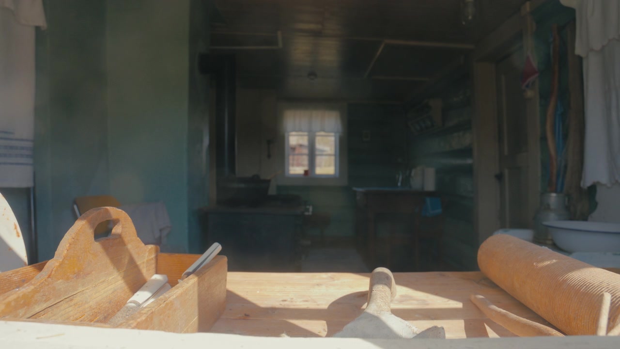 La calda luce del sole illumina vecchi utensili da forno su un tavolo di legno, mentre una cucina rustica e fioca si estende dietro di essi, creando una scena domestica nostalgica.