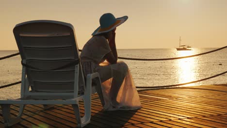 a woman looks at the sunrise over the sea. sits on a sunbed, in the distance a fishing boat is visible. scenic dawn landscape