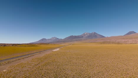 Carretera-Desértica-Que-Atraviesa-Un-Vasto-Y-Tranquilo-Paisaje-Del-Altiplano-En-Chile,-Bajo-Un-Cielo-Azul-Claro.