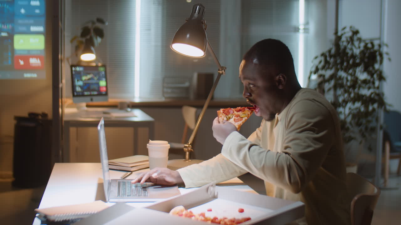 Forretningsmand spiser pizza og arbejder på kontoret om natten