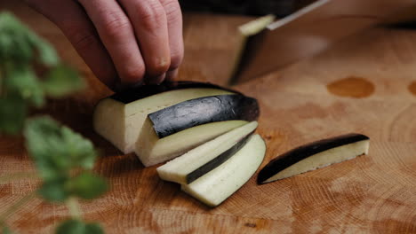 chef masculino cortando berenjena en rodajas finas en la cocina en una tabla de cortar de madera en la cocina