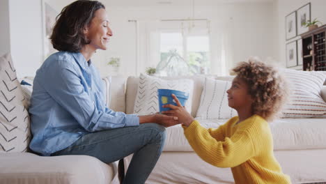 Pre-teen-African-American-girl-giving-her-mum-a-homemade-painted-plant-pot-as-a-gift,-side-view