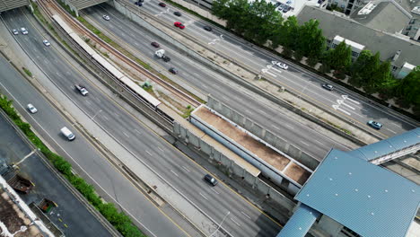 Blick-Aus-Der-Vogelperspektive-Auf-Stark-Befahrene-Mehrspurige-Autobahnen-Und-U-Bahnen,-Die-In-Der-Mitte-Auf-Gleisen-Vorbeifahren