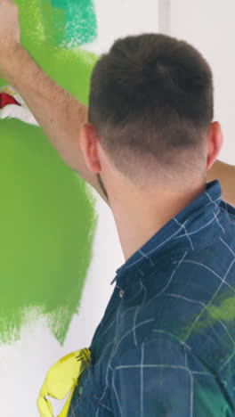 positive bearded man in dirty blue shirt with attractive blonde woman paint wall bright green color in repairing room