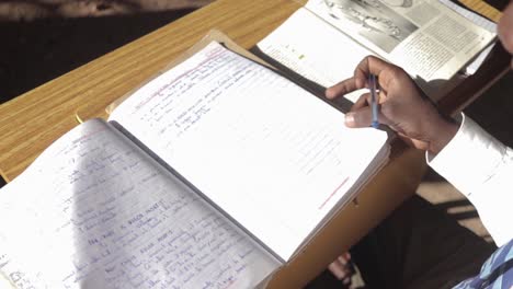 A-slow-motion-shot-of-a-young-African-mans-hands-as-he-flips-the-pages-of-his-note-book-while-sitting-in-a-run-down-school-in-Africa