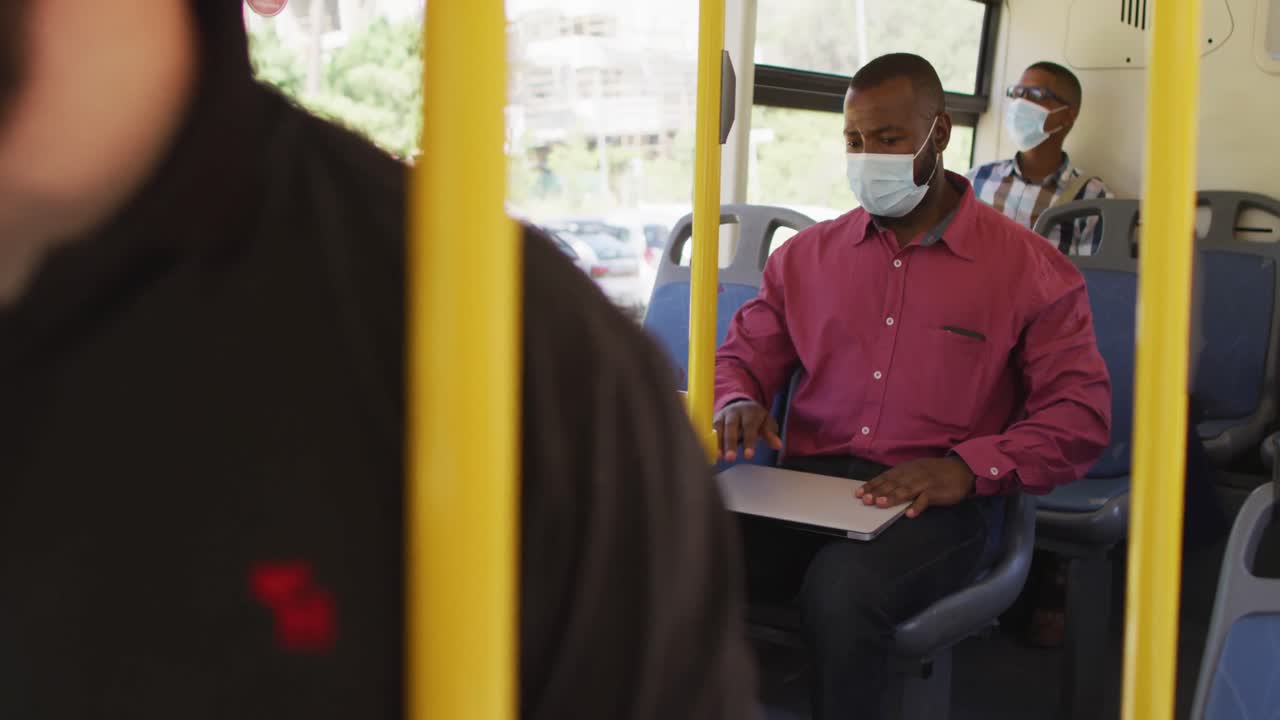 Afroamerikansk mand i byen med ansigtsmaske, bruger bærbar computer i bus