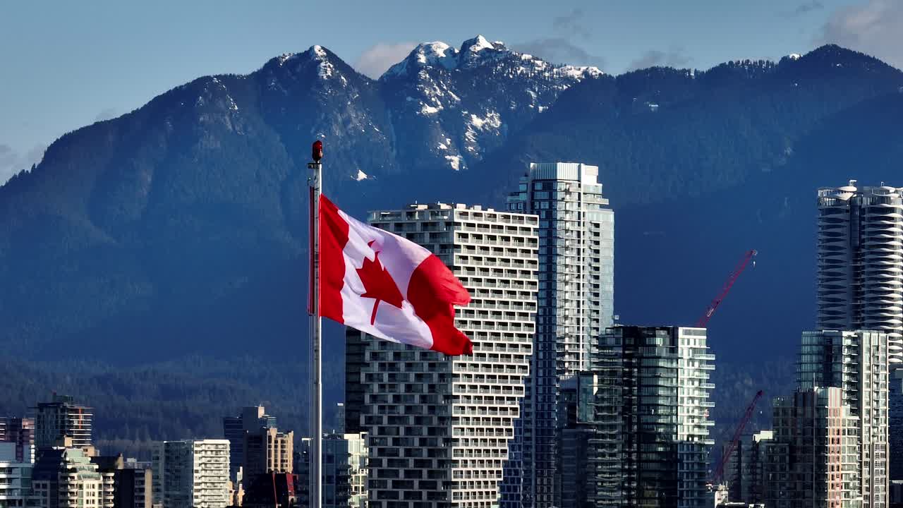 The Canadian Flag Stands Tall Against a Striking City Skyline and Mountain Backdrop in Vancouver, Canada - Zoom In Shot