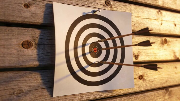 Practice shot landing third arrow into paper target by red bullseye on wall, casting long shadows