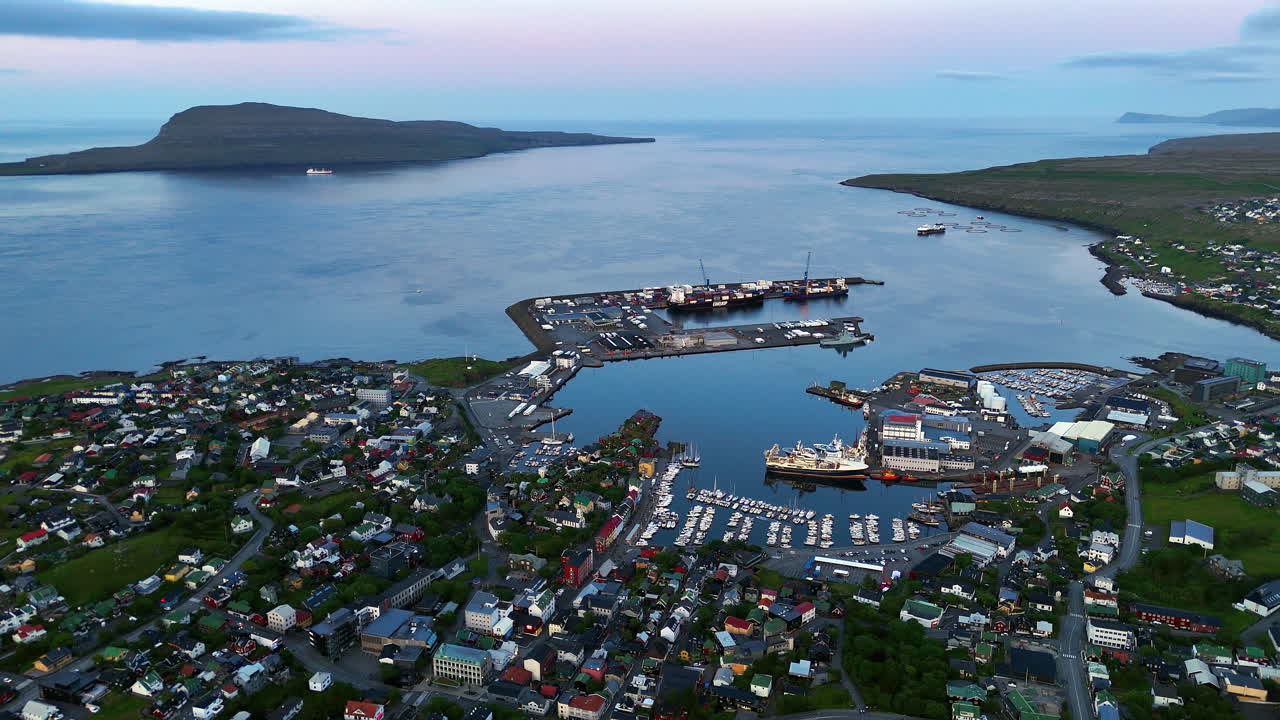 Cinematic aerial view of torshavn harbor in faroe islands with fishing boats, colorful houses, shipping port and dramatic coastline under soft evening light