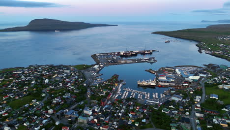 cinematic aerial view of torshavn harbor in faroe islands with fishing boats, colorful houses, shipping port and dramatic coastline under soft evening light