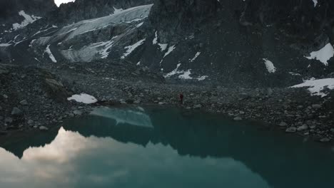 male hiker standing in awe of the rugged alaskan mountain range with epic reflection shot on drone from a distance