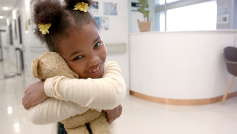 portrait of happy african american girl hugging mascot in hospital, slow motion