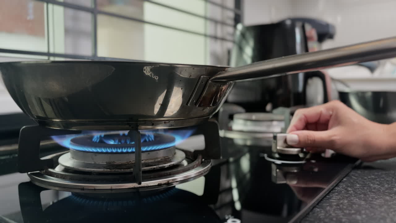 Người phụ nữ bật bếp ga và vặn nhỏ lửa trong bếp gia đình. Quá trình nấu ăn hàng ngày, cảnh sinh hoạt gia đình, chuẩn bị bữa ăn trong nhà