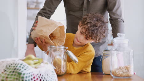 father helping son to refill food containers at home using zero waste packaging