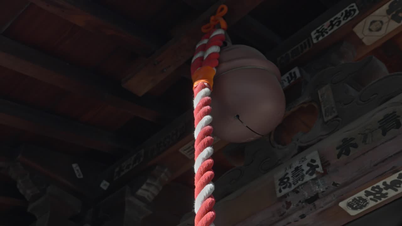 A large temple bell hangs from a wooden structure, its rope ready to be pulled, echoing ancient traditions and spiritual practices.