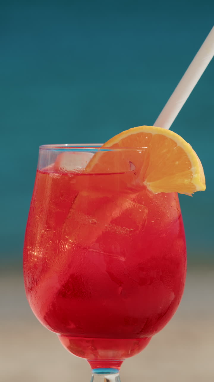 Close up of a refreshing red orange cocktail with orange slice and ice cubes, captured outdoors on a sunny day in Cannes. Vertical