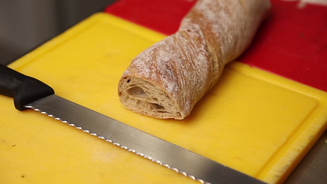 Baguette fresca e coltello seghettato su un tagliere giallo
