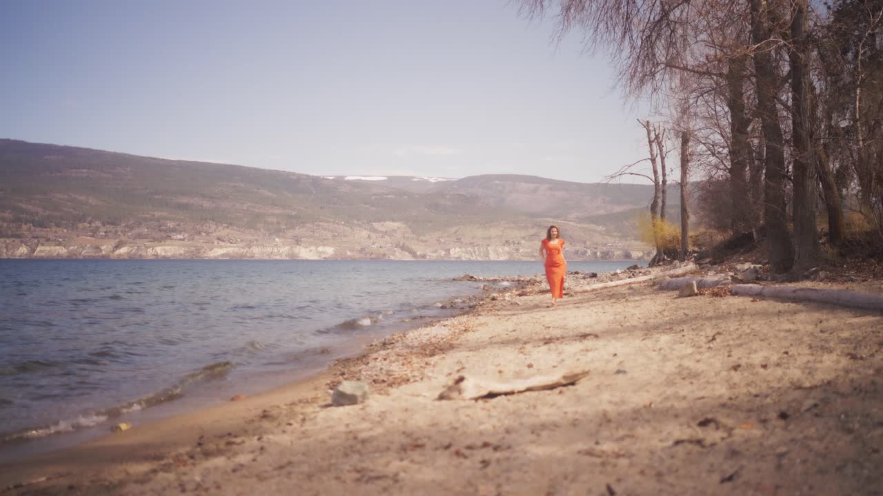 Girl in red dress approaching in slow motion along beach on windy day