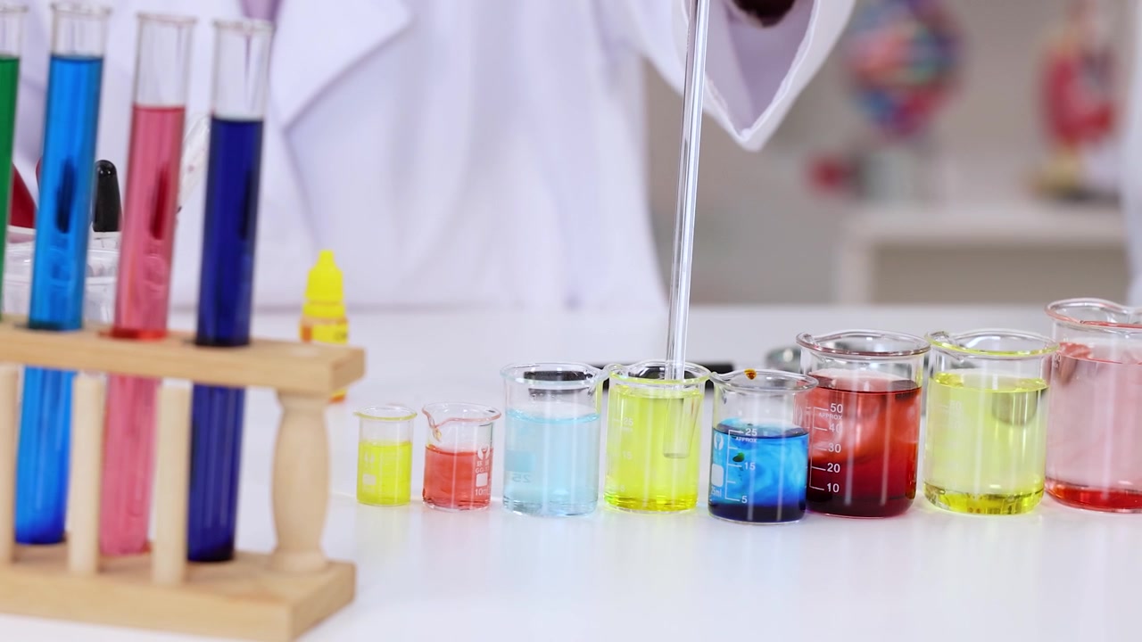 Uno scienziato in camice bianco usa una pipetta per mescolare soluzioni chimiche vivaci