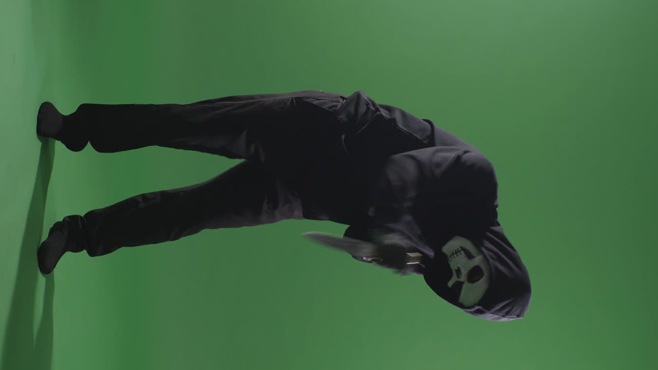 hombre aterrador en la sudadera con capucha usando máscara de halloween apuñalando con un cuchillo por hacer un gesto amenazante en el fondo de la pantalla verde