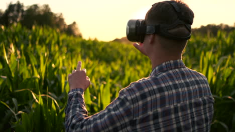 a modern farmer in a vr helmet drives a corn crop standing in a field at sunset in the sun. the concept of smart fields of use of neural networks in agriculture. the use of artificial intelligence to agriculture and harvest