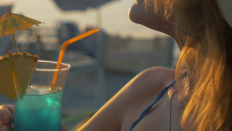 young woman having cocktail on beach at sunset