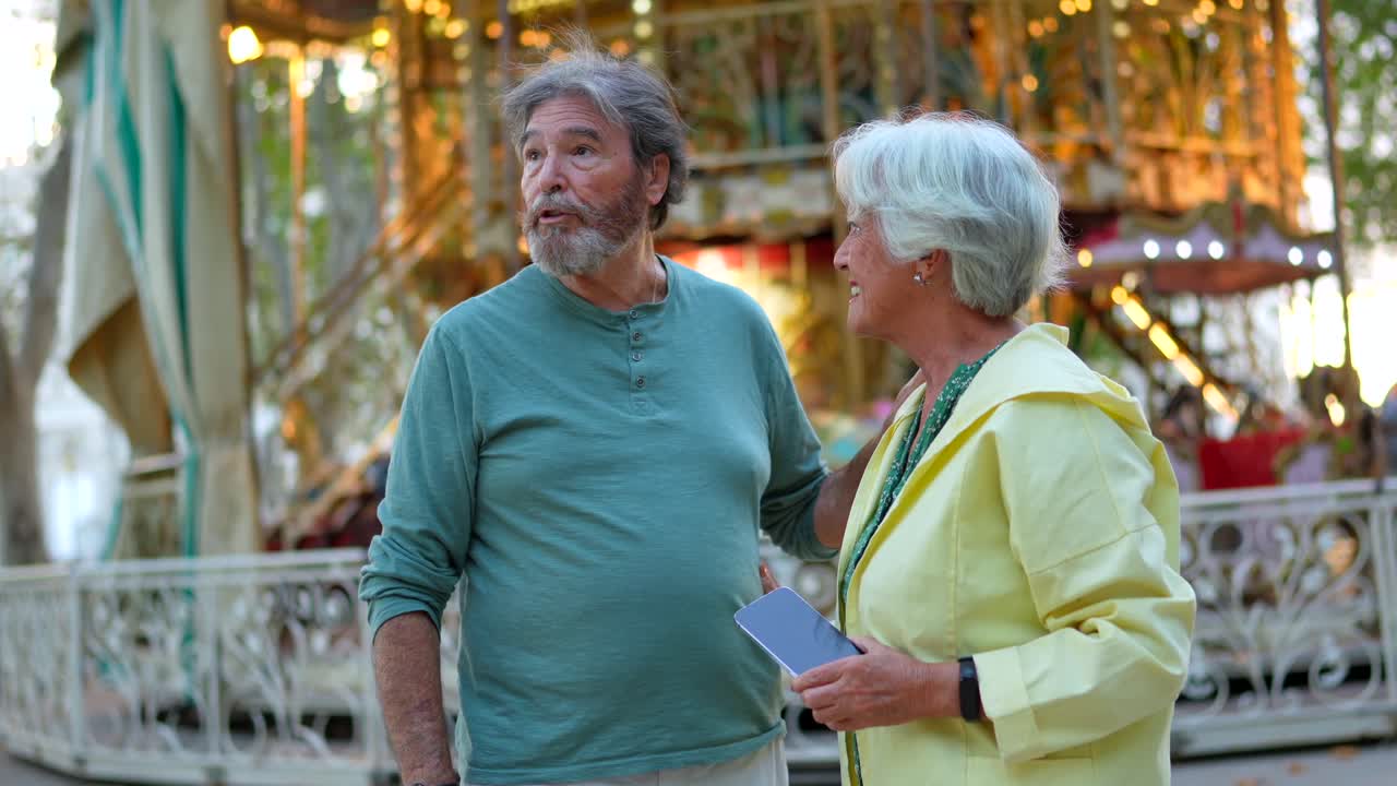 Senior couple taking a selfie in front of a carousel