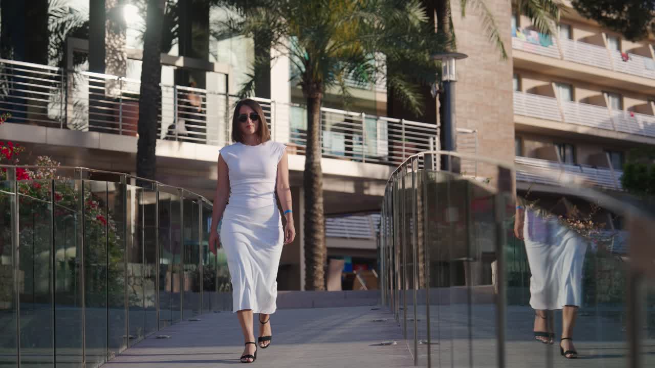 una mujer con un vestido blanco camina por el puente del hotel de la playa de cala vines, mallorca.