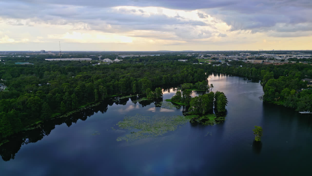 Aerial across deep blue river bordered by dense green forest in Tampa, Florida, sunset cloud textures reflect in water
