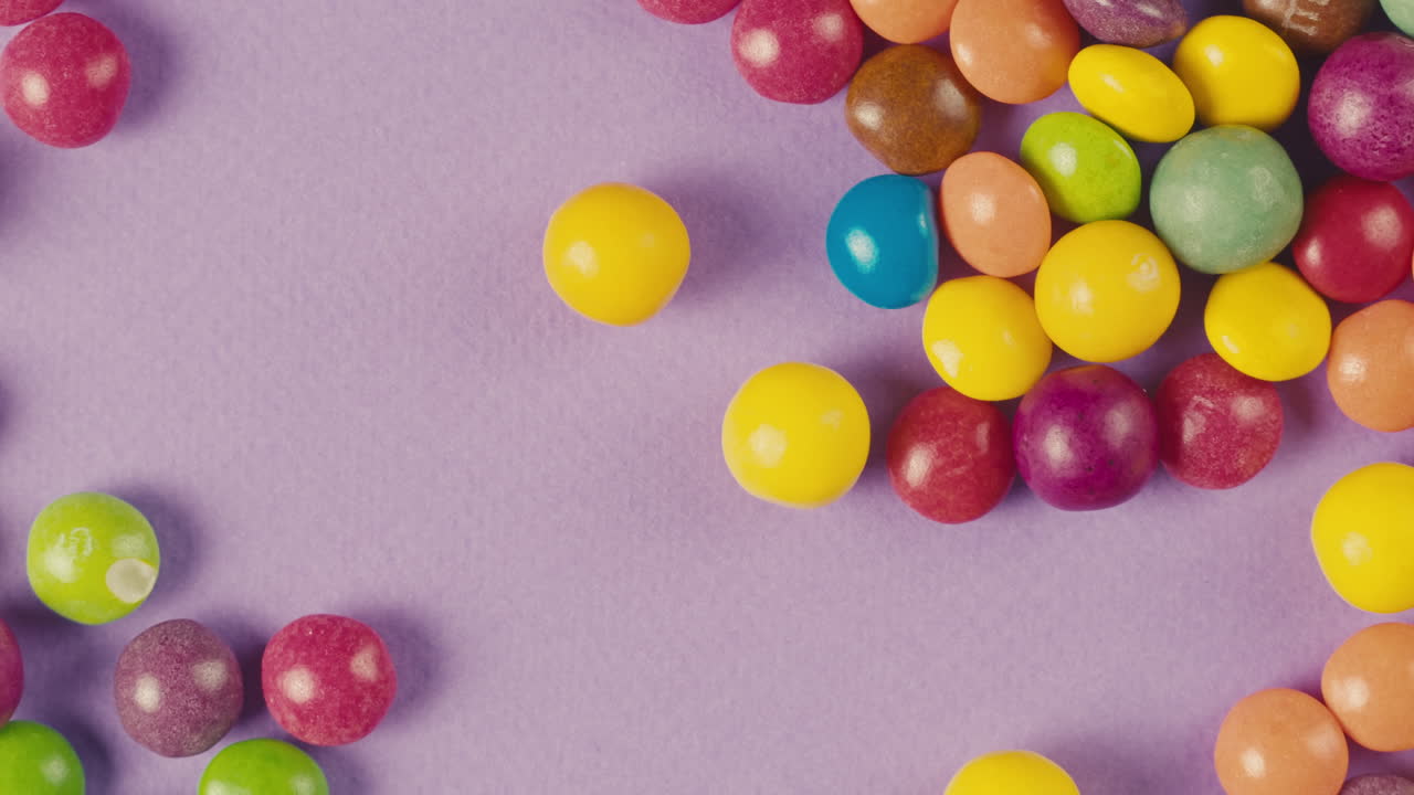 Colorful dragee candies lollipops on purple background. Woman hands moove the bonbons. Summer bright texture studio shot for store, supermarket, close-up top view. Children sweets made of sugar.