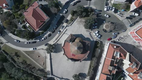 sunny aerial view of lisbon church's red roof tiles with passing cars at a roundabout and green trees