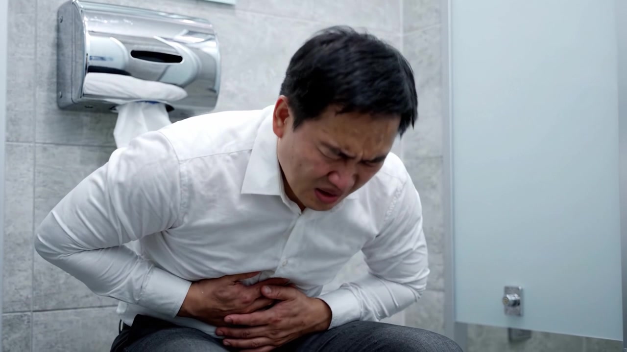 Struggling with Discomfort: A Depiction of an Individual Experiencing Intense Pain While Seated in a Bathroom Stall, Highlighting the Challenges of Digestive Distress.