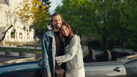 Una-Hermosa-Pareja-De-Un-Chico-Y-Una-Chica-Morena-Están-De-Pie-Y-Posando-Contra-El-Fondo-De-Su-Cabriolet-Gris,-Son