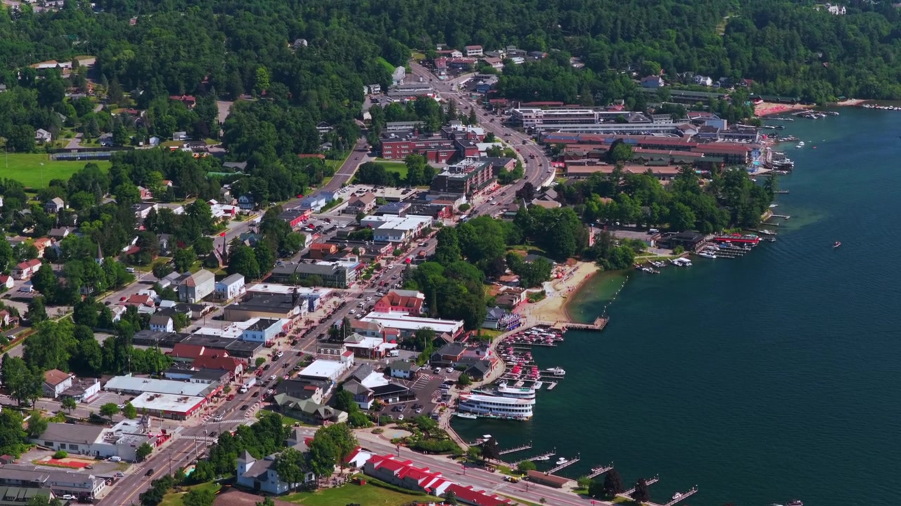 Città di Lake George nella parte settentrionale dello Stato di New York, vista aerea con drone, estate, centro, Main Street, auto, traghetti, barche, strada, edifici, paesaggio, mattina soleggiata, cielo blu, movimento di parallasse circolare con panoramica verso l'alto.