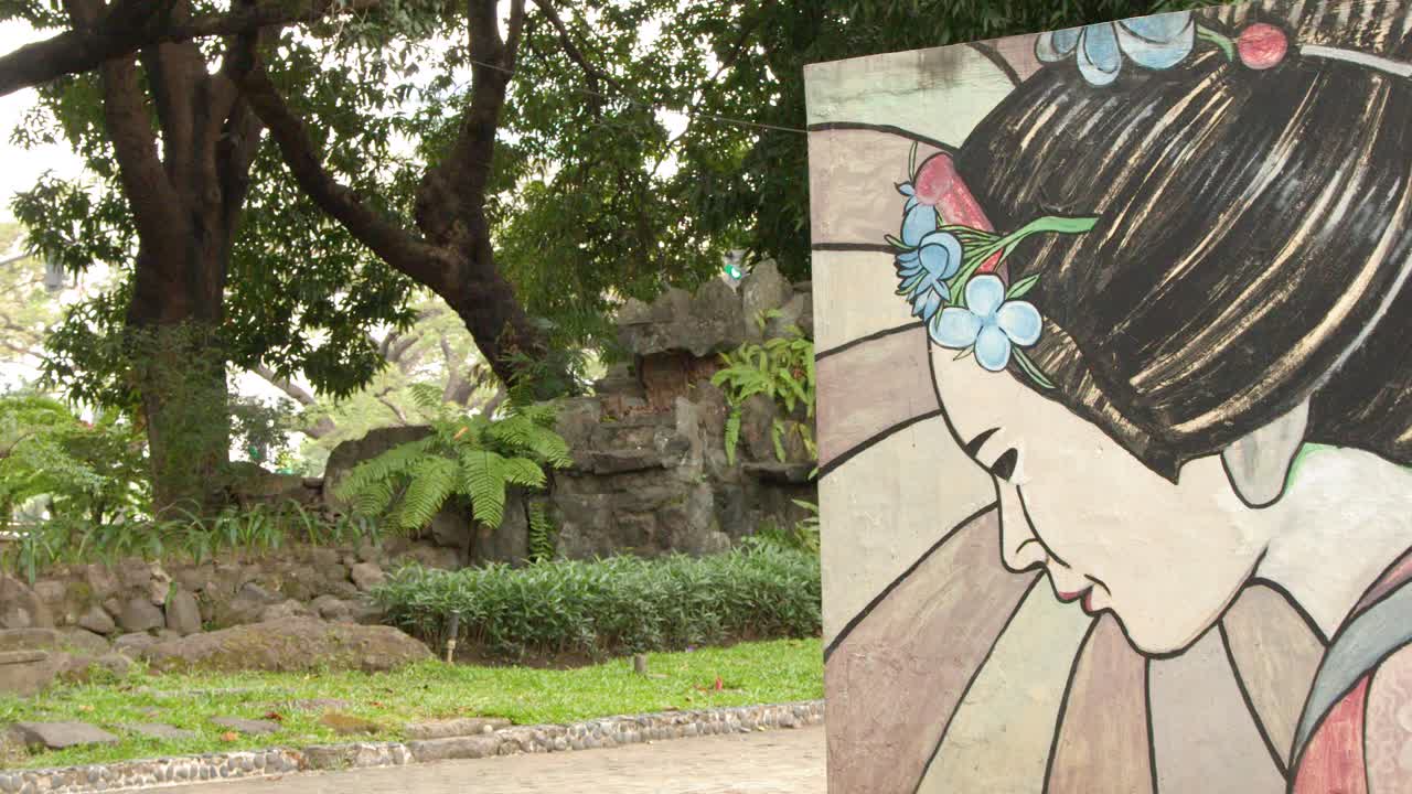 Ripresa statica di un murale di geisha su un muro di pietra all'interno di un verde giardino tropicale