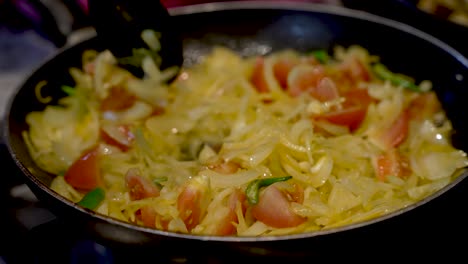 una toma en cámara lenta de cerca de una sartén mientras un chef revuelve cebollas picadas, tomates picados y chiles alrededor de una sartén caliente para asegurarse de que las verduras se cocinen uniformemente