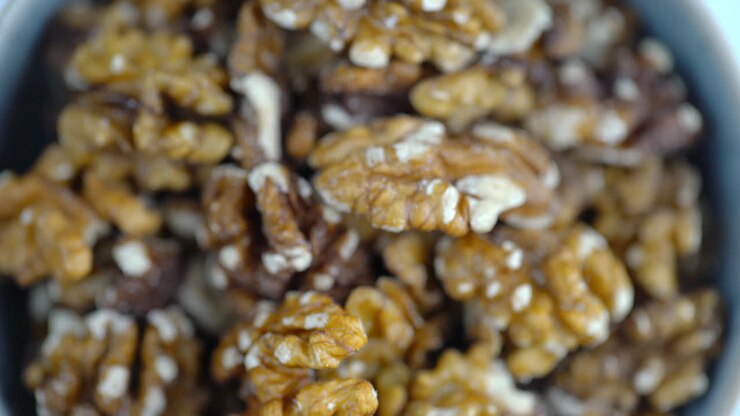 Noci che ruotano in una ciotola. Primo piano macro 4K di noci che girano. Noci e cibo su sfondo bianco. Cibo vegano crudo a base vegetale ricco di proteine. Alimenti sani e vegetariani. Ingredienti per una colazione sana
