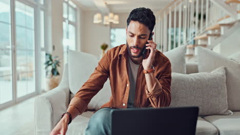 man talking on the phone while working on his laptop at home