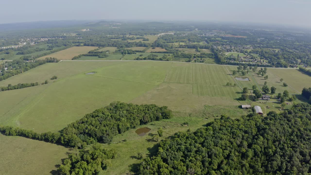 4k aerial panning around southern farm with open green fields and small pond