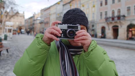 senior man taking pictures with photo camera, using retro device outdoors in winter city center