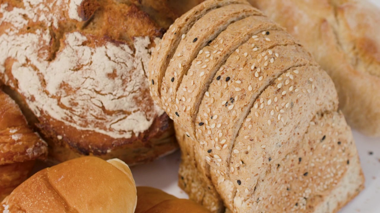 Slow camera pan across various artisan loaves, croissants, and sliced whole grain breads.