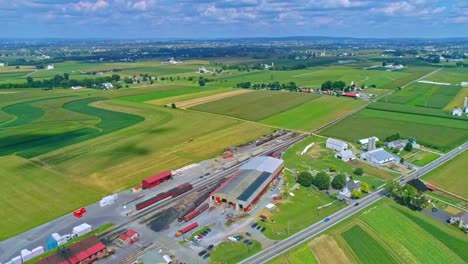 an aerial traveling view of corn fields and harvesting crops, with a train yard and patches of color on a beautiful summer day