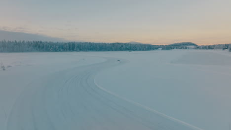 Aerial-view-chasing-Norbotten-driver-drifting-corners-on-frozen-Lapland-ice-lake-at-sunrise