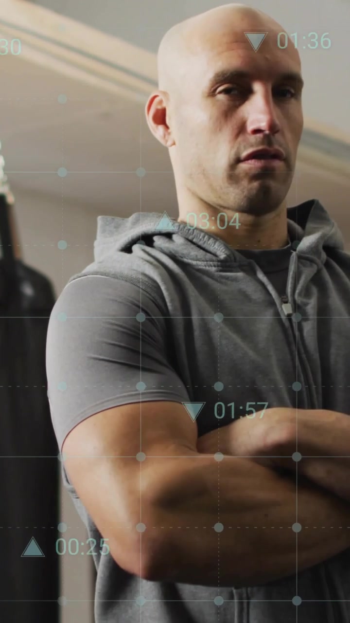 Vertical video: Coach standing arms crossed in gym, HUD activating, cycling timers tracking fitness