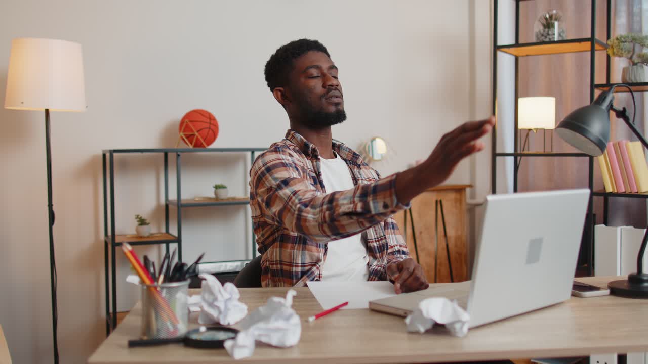 Sad young man working at home office crumples throwing heets of paper with bad ideas and mistakes
