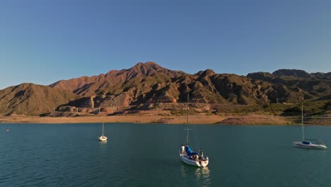 aeril dolly shot past a group of sailboats floating in a lake in mendoza, argentina