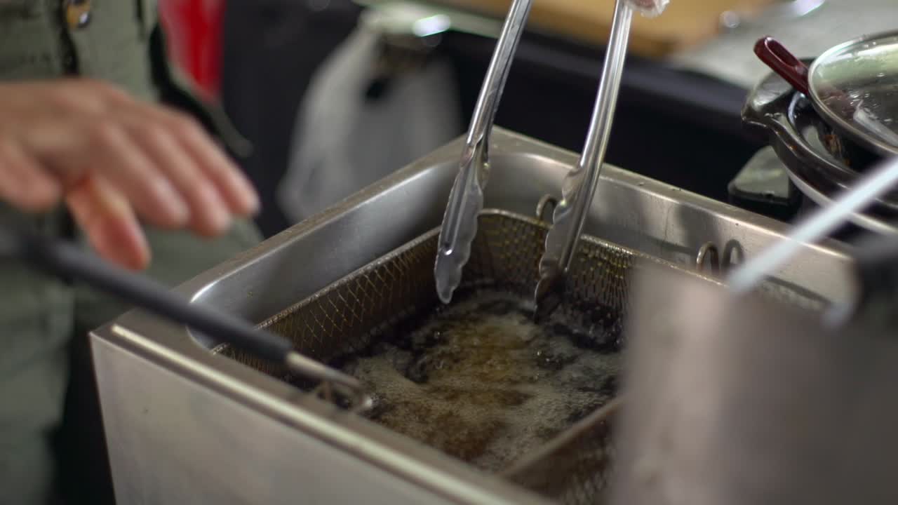 Köttbullar rörs om med tång i ett kar med kokhet olja, filmat som en närbild i handhållen slow motion-stil